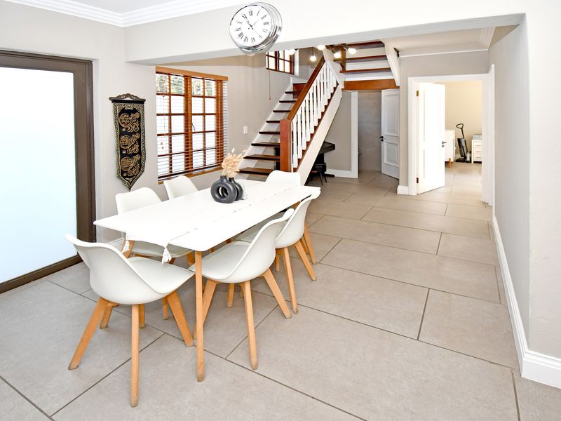 Open-plan dining area featuring large format floor tiles, a wooden staircase with white balustrades, and direct access to the exterior via a sliding door.