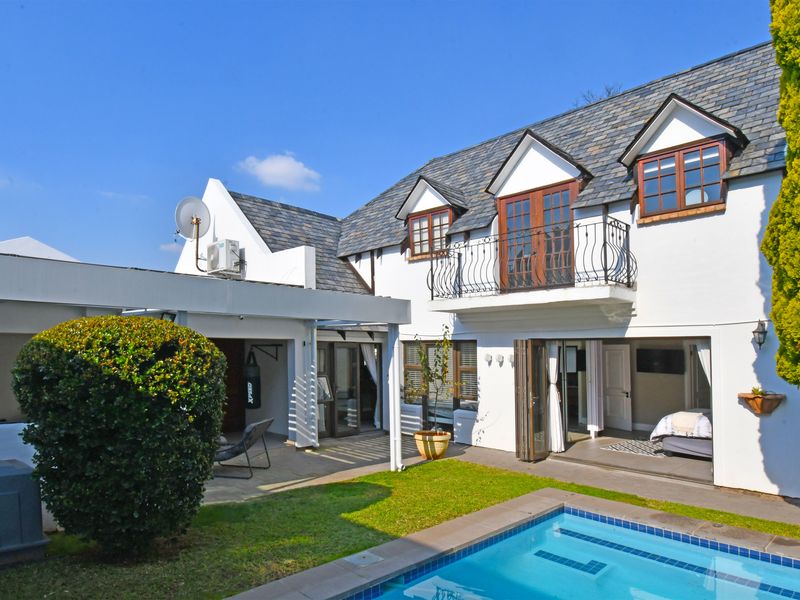Rear view of the property featuring a swimming pool, covered patio area, and a balcony with wrought iron railings overlooking the garden.