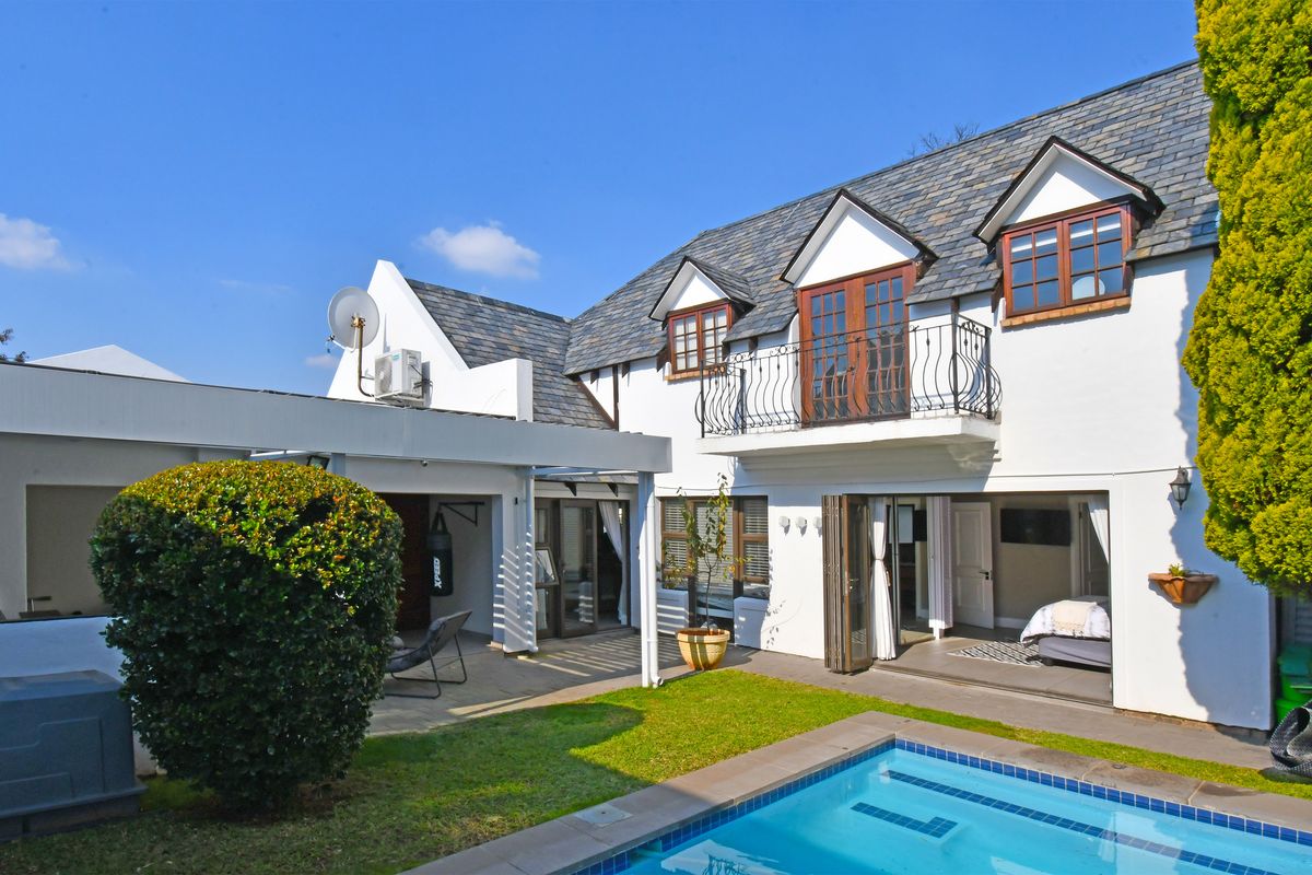 Rear view of the property featuring a swimming pool, covered patio area, and a balcony with wrought iron railings overlooking the garden.