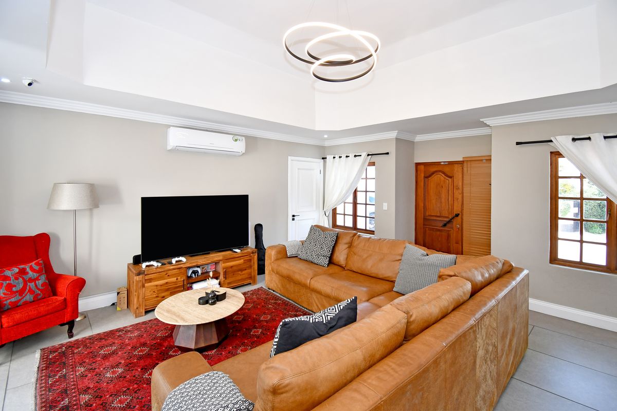 Spacious living room featuring a tray ceiling, crown molding, tiled flooring, and a wall-mounted split-system air conditioner.