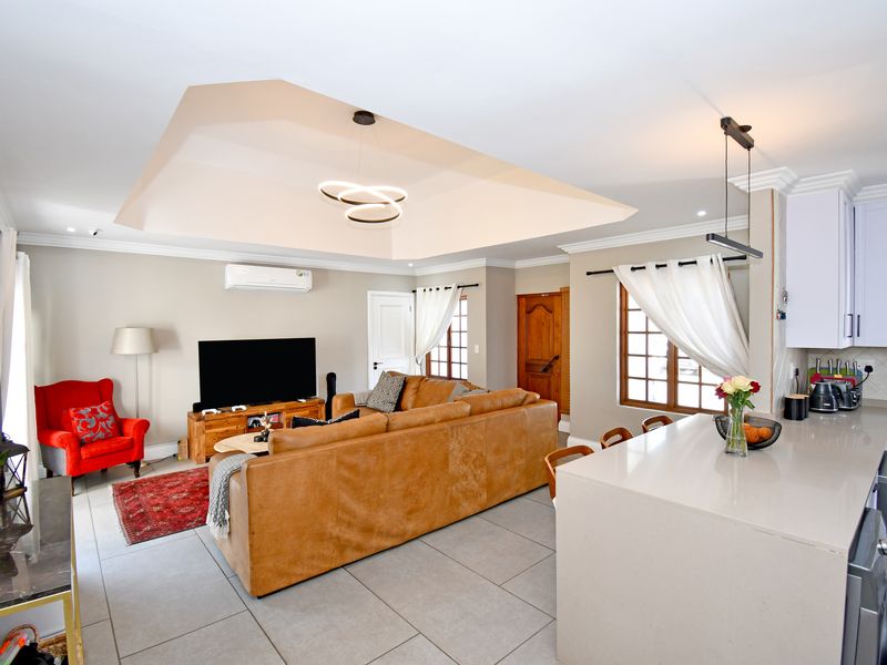 Spacious open-plan living area featuring a tray ceiling, modern lighting, tiled floors, and a contemporary kitchen with a central island and quartz countertops.