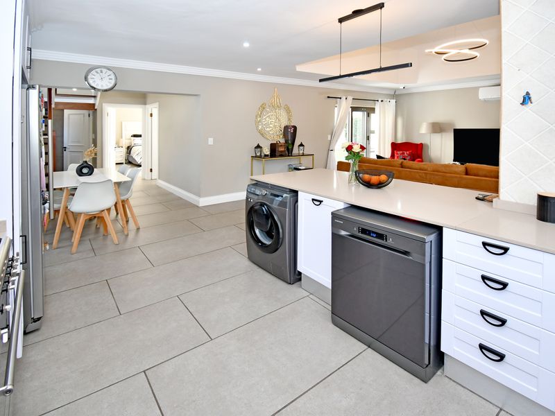 Modern open-plan kitchen and living area featuring stone countertops, integrated appliances, tiled flooring, and contemporary lighting fixtures.