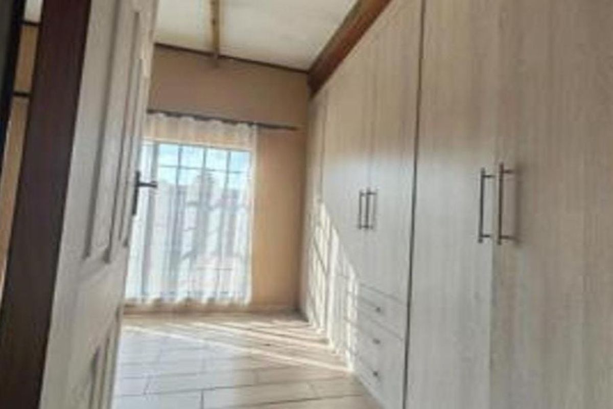 A bedroom featuring extensive built-in cupboards, tiled flooring, and natural light through a window with security bars.