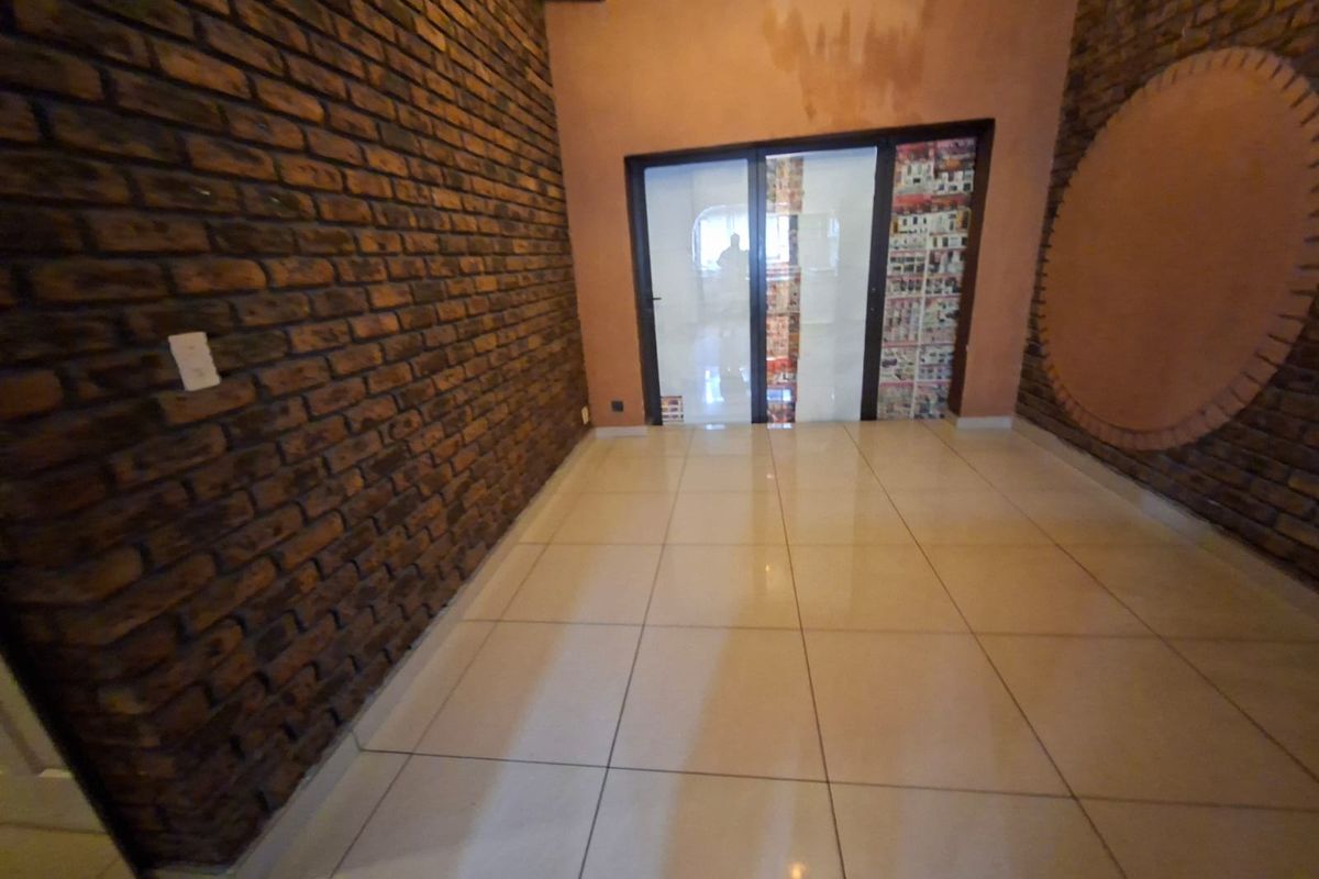 Empty living area featuring exposed brick walls, large format floor tiles, and a glass sliding door leading to an adjacent space.