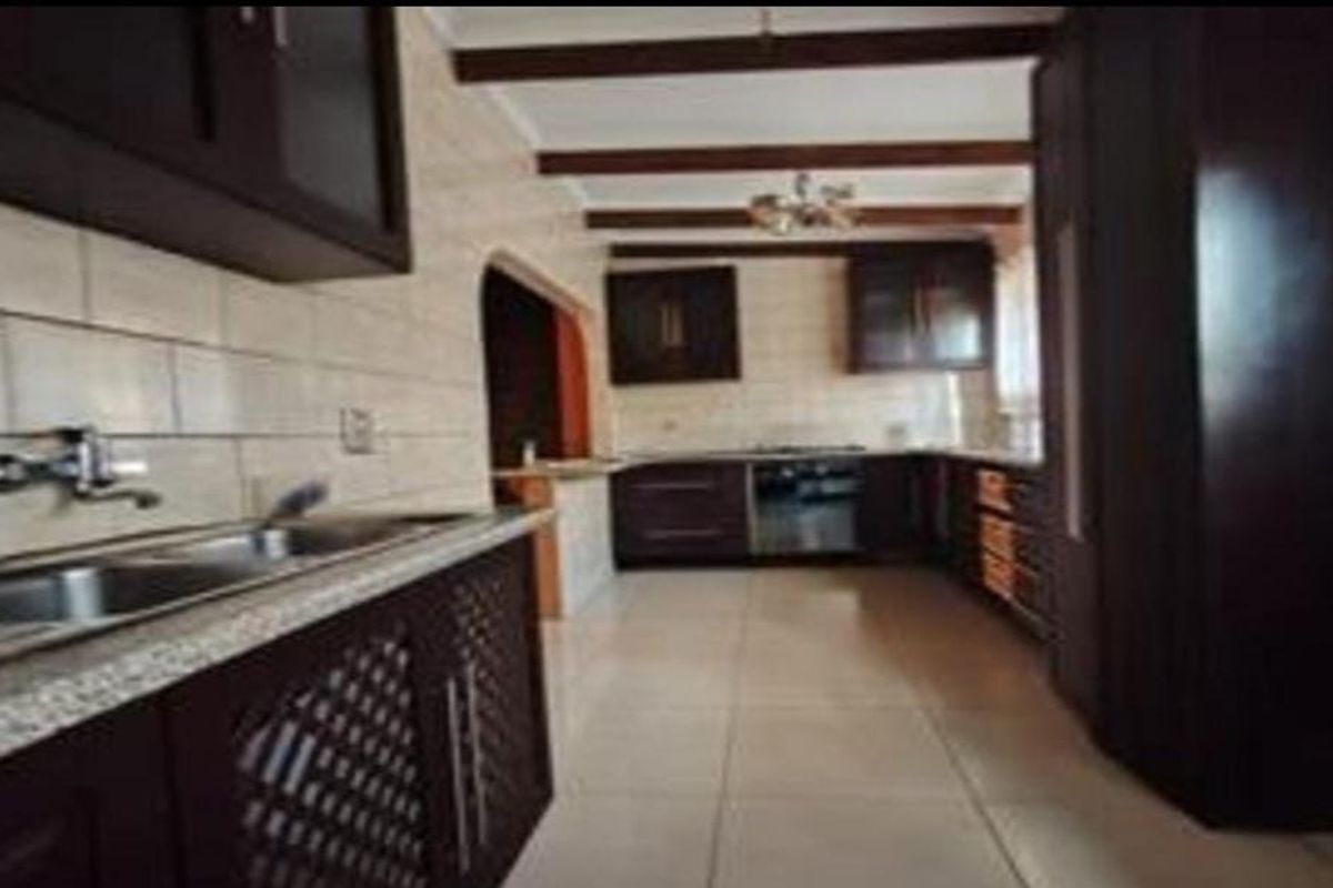 Spacious kitchen featuring dark wood cabinetry, granite countertops, double basin sink, and exposed ceiling beams, offering a functional layout with ample storage.