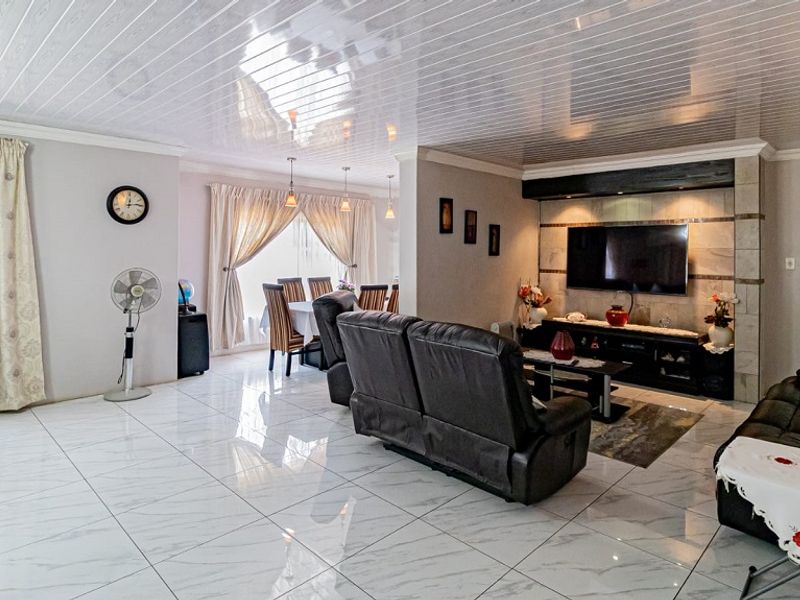 Spacious open-plan living and dining area featuring glossy tiled floors, a modern PVC ceiling, and a built-in media wall with integrated lighting.