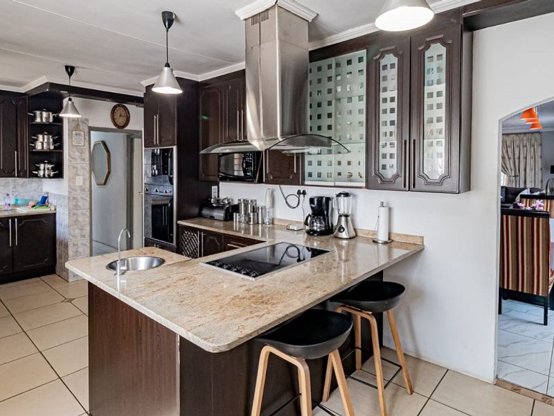Spacious kitchen featuring dark wood cabinetry, granite countertops, a central island with a built-in hob, and modern stainless steel appliances.