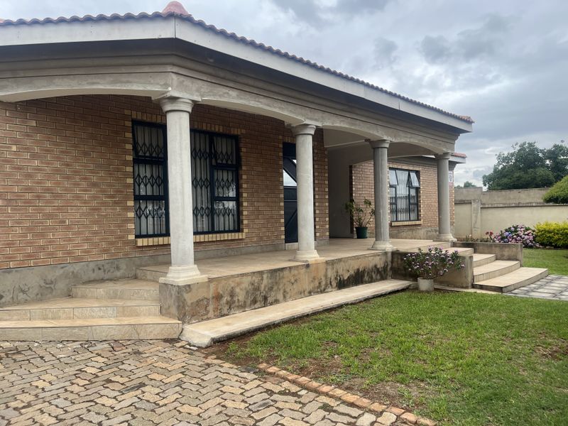 A front exterior view of a brick house featuring a covered patio with concrete columns, security bars on windows, and a paved driveway.