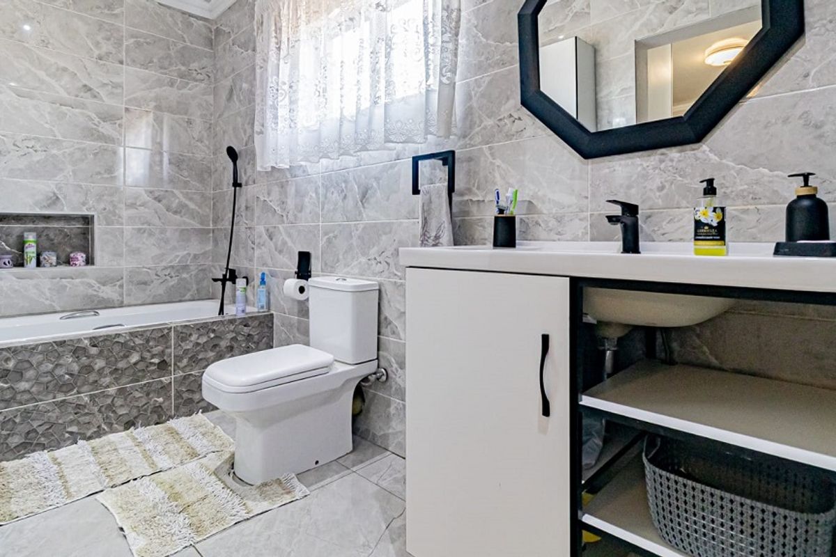 Modern bathroom featuring floor-to-ceiling marble-look tiling, a built-in bathtub with a recessed niche, a contemporary vanity unit, and a sleek toilet.