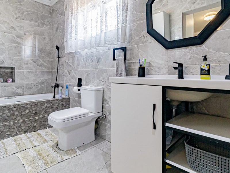 Modern bathroom featuring floor-to-ceiling marble-look tiling, a built-in bathtub with a recessed niche, a contemporary vanity unit, and a sleek toilet.