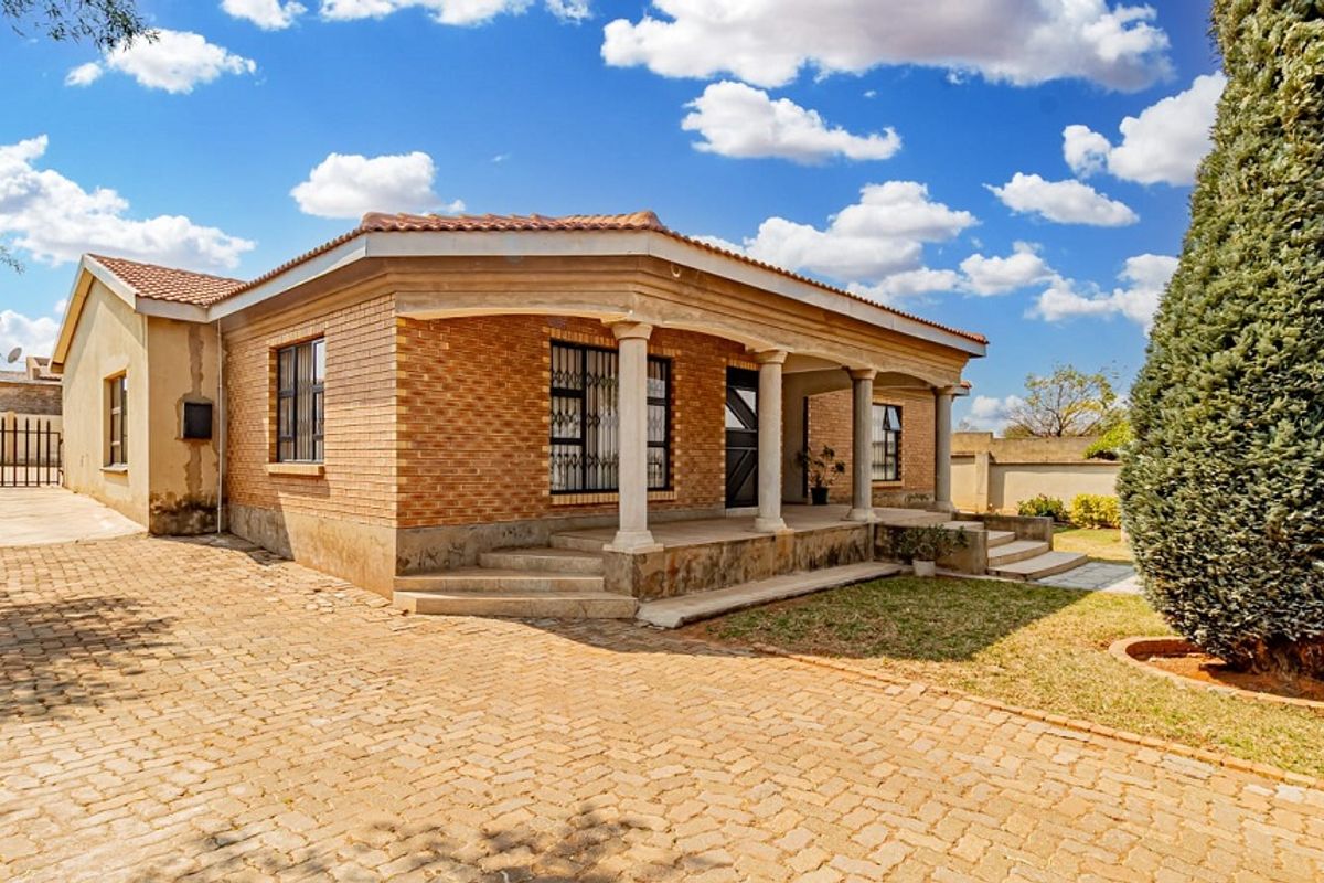 Front view of a single-story brick house featuring a covered porch with concrete columns, a paved driveway, and established garden surroundings.