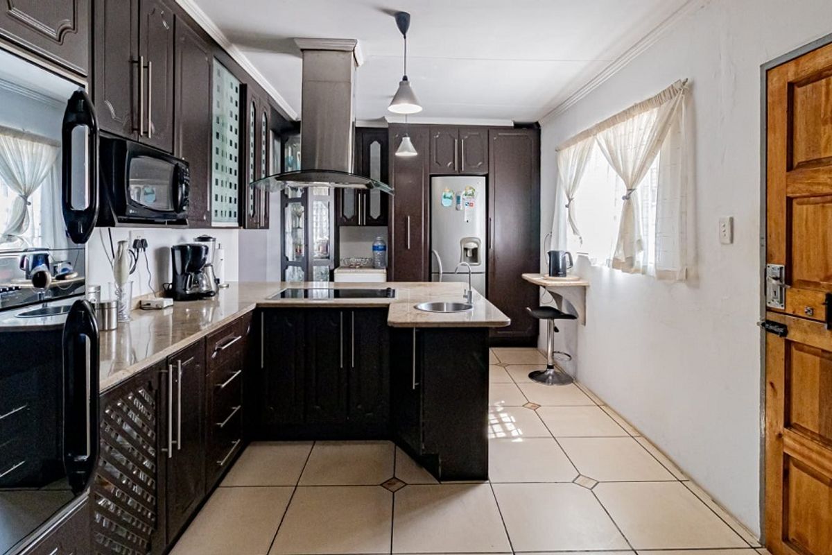 A well-appointed kitchen featuring dark wood cabinetry, stone countertops, integrated appliances, and a breakfast bar, finished with ceramic tile flooring.
