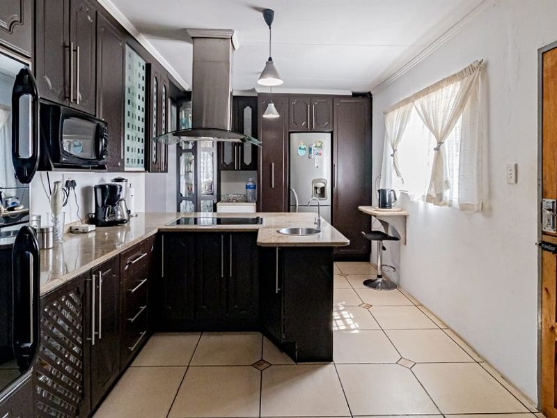 A well-appointed kitchen featuring dark wood cabinetry, stone countertops, integrated appliances, and a breakfast bar, finished with ceramic tile flooring.