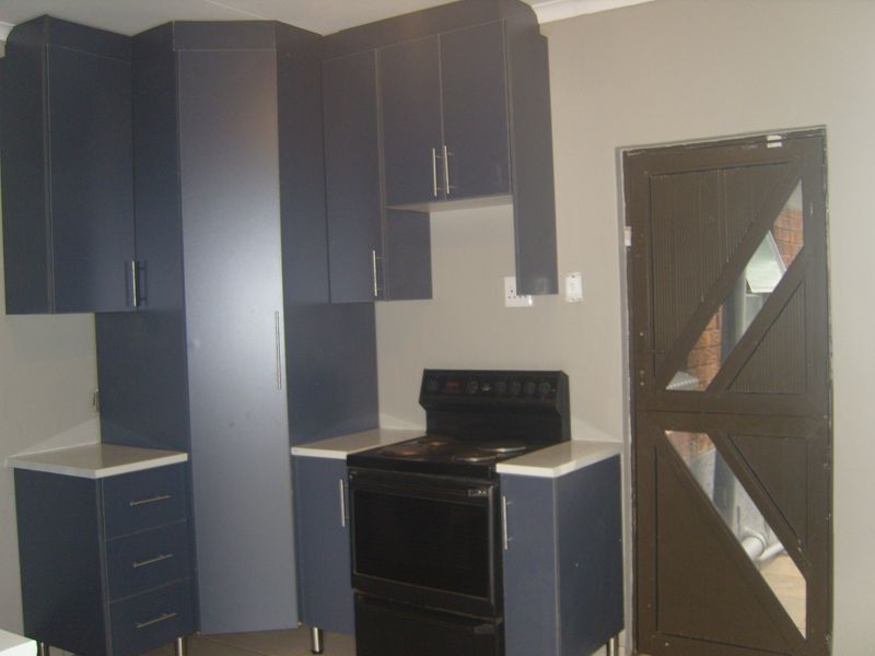 A functional kitchen area featuring dark blue cabinetry, white countertops, and a freestanding stove, with direct access to an external door.