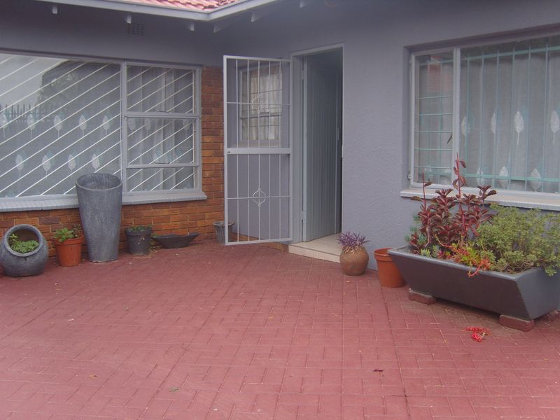 A paved outdoor patio area featuring a security gate entrance, brick and rendered wall finishes, and security bars on the windows.