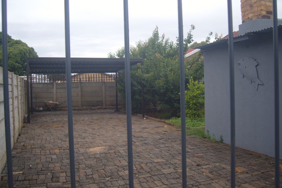 Rear exterior area featuring a paved driveway, a covered carport, and a precast concrete boundary wall.