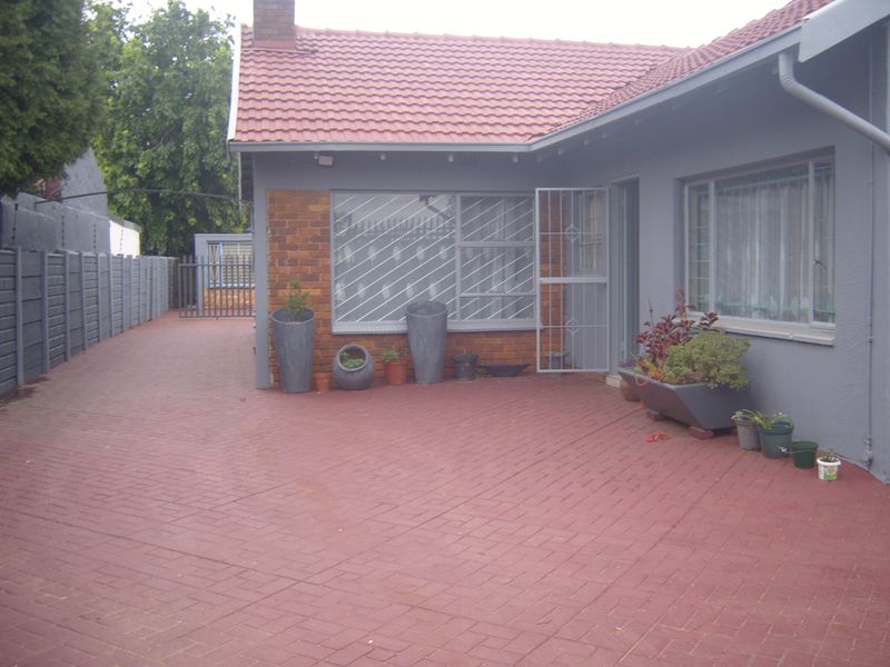 A paved rear courtyard area featuring a brick and rendered facade, tiled roof, and security bars on windows and doors.
