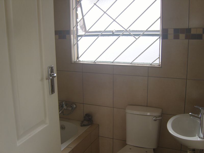 A functional bathroom featuring tiled walls, a built-in bathtub, a standard toilet, and a washbasin with a modern mixer tap.