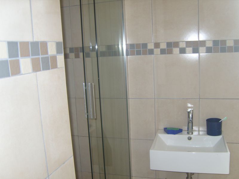 A compact bathroom featuring a wall-mounted basin with a chrome mixer tap and a glass-enclosed shower with neutral ceramic wall tiling.