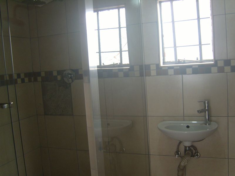 A compact bathroom featuring a shower enclosure, wall-mounted basin, and tiled walls. The space requires minor repairs to finishes and plumbing.