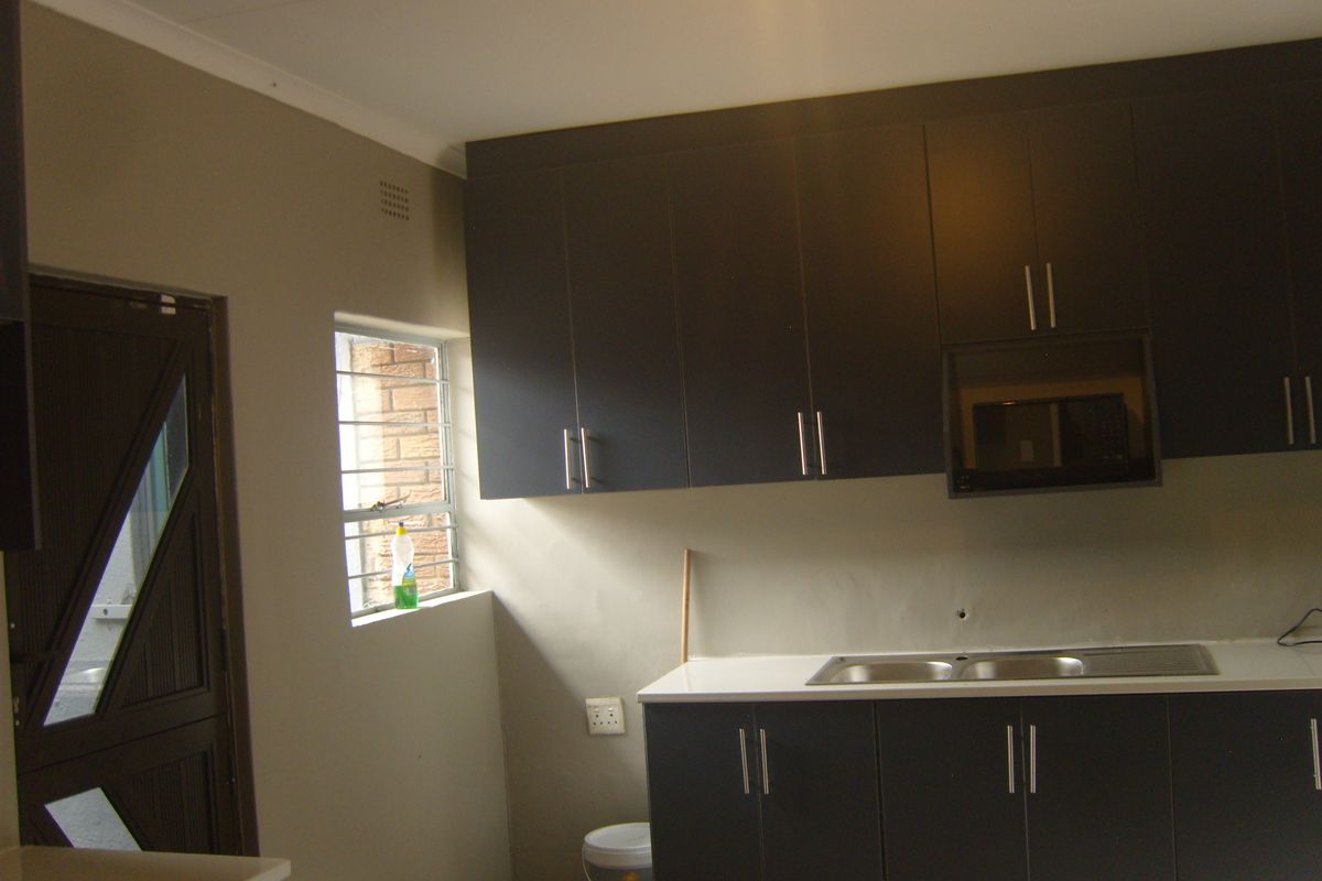 A functional kitchen featuring dark cabinetry, a built-in microwave, a stainless steel sink, and a white countertop with a window providing natural light.