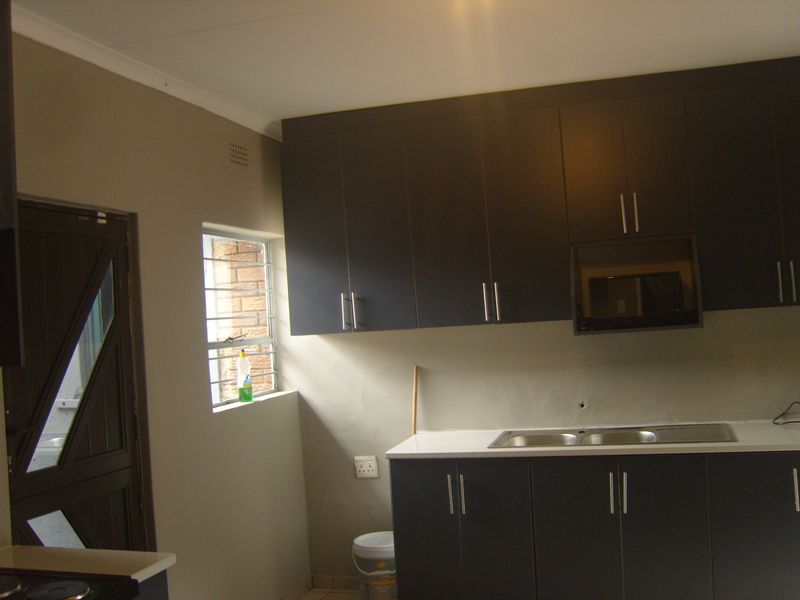 A functional kitchen featuring dark cabinetry, a built-in microwave, a stainless steel sink, and a white countertop with a window providing natural light.