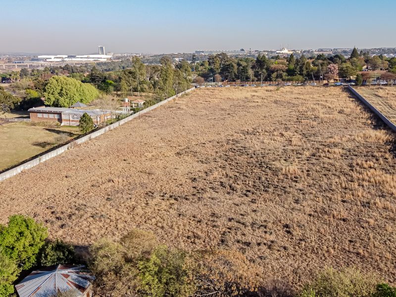 An aerial view of a large, vacant residential plot enclosed by perimeter walls, situated in an established suburban area.