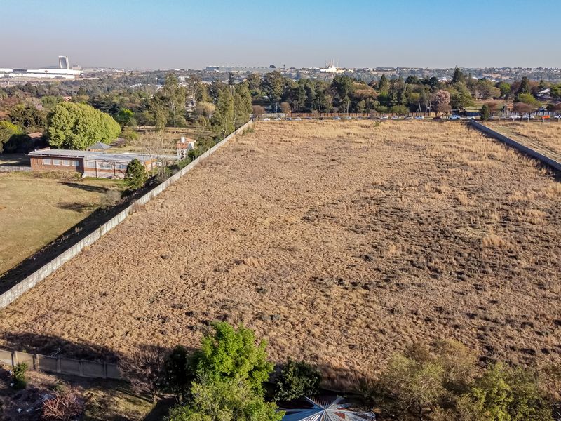 An aerial view of a large, vacant residential plot enclosed by perimeter walls, offering a clear perspective of the land and surrounding neighborhood.