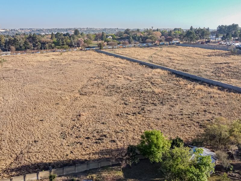 An aerial view of a large, vacant residential plot featuring perimeter walling and dry grass, suitable for future development.
