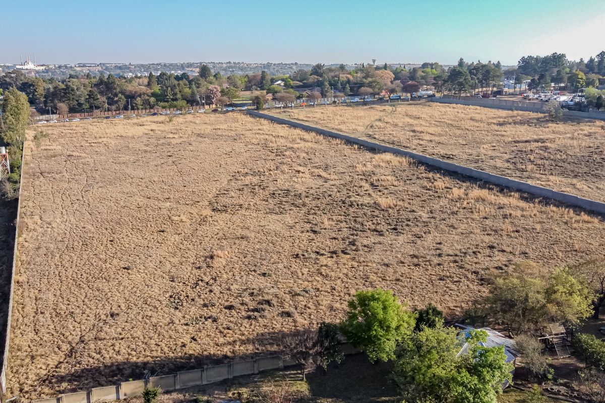 An aerial view of a large, vacant residential plot featuring perimeter walling and dry grass, suitable for future development.