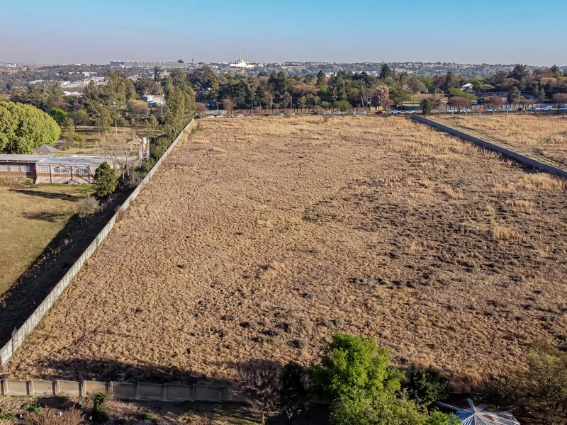 An aerial view of a large, vacant residential plot enclosed by perimeter walls, offering a clear perspective of the land and surrounding area.