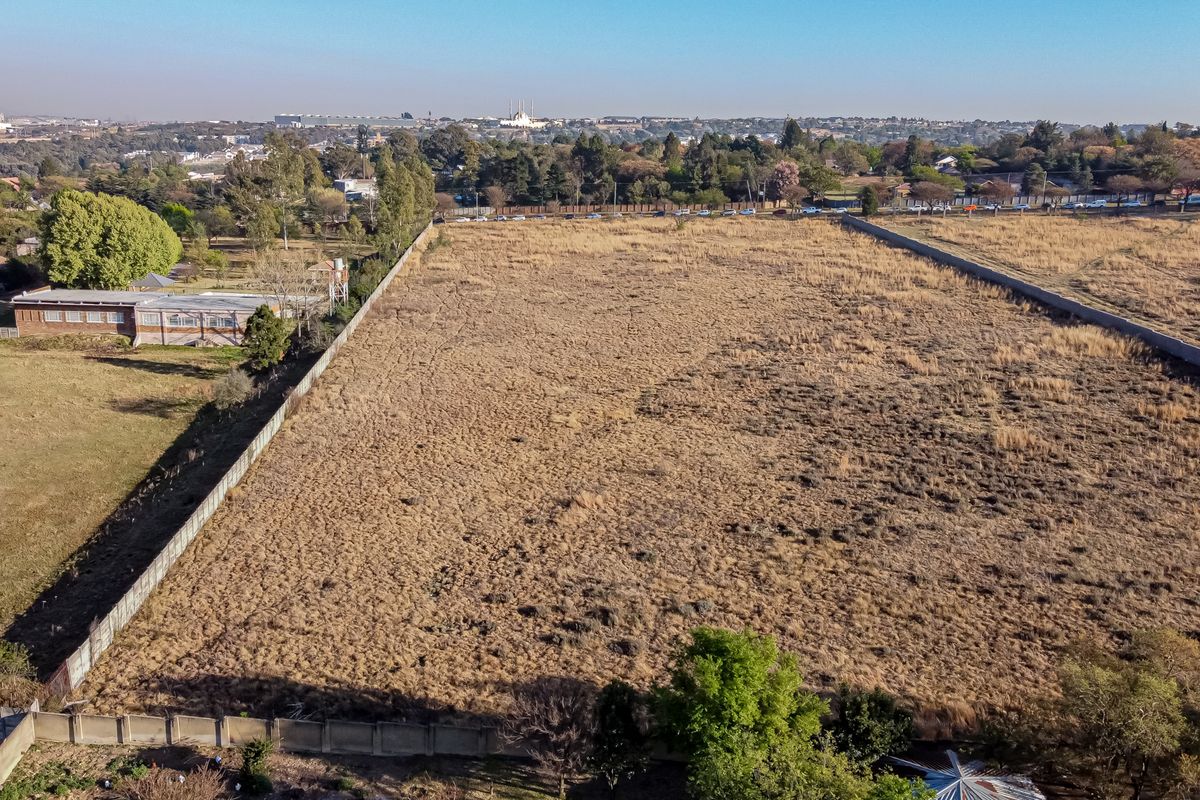 An aerial view of a large, vacant residential plot enclosed by perimeter walls, offering a clear perspective of the land and surrounding area.