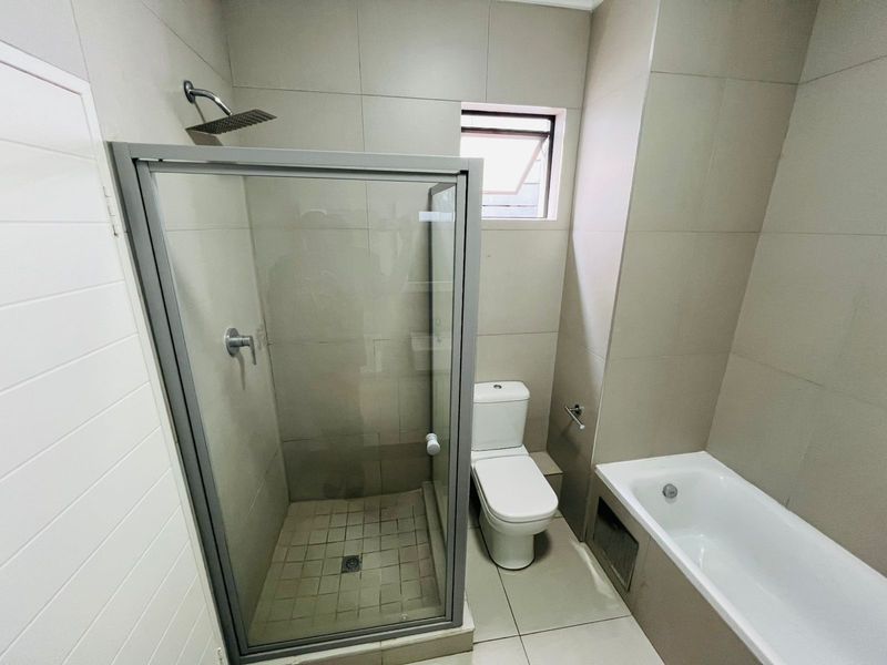 Modern bathroom featuring a glass-enclosed shower, a separate bathtub, and a toilet with neutral floor-to-ceiling tiling.