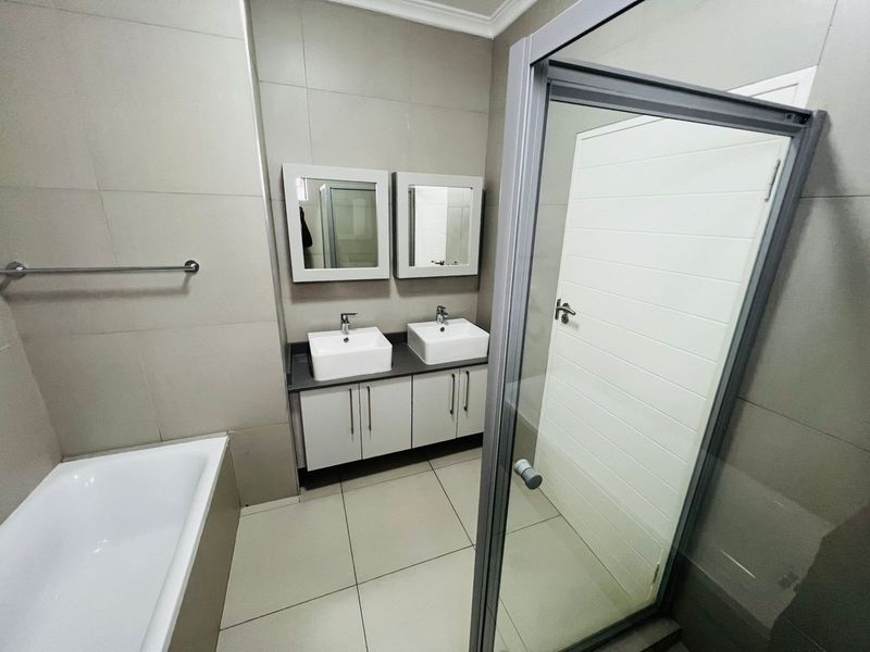 Modern bathroom featuring a double vanity with vessel sinks, a separate bathtub, and a glass-enclosed shower with neutral wall and floor tiling.