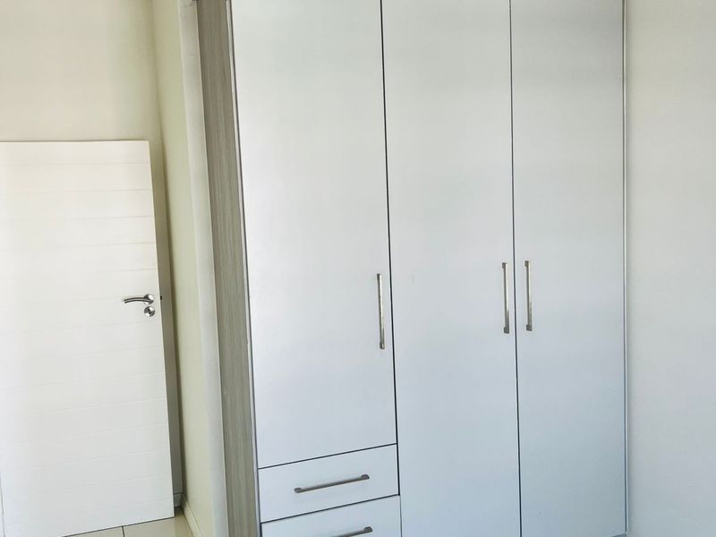 A bedroom featuring a modern, built-in wardrobe with integrated drawers and a neutral finish, complemented by tiled flooring and a clean, minimalist aesthetic.