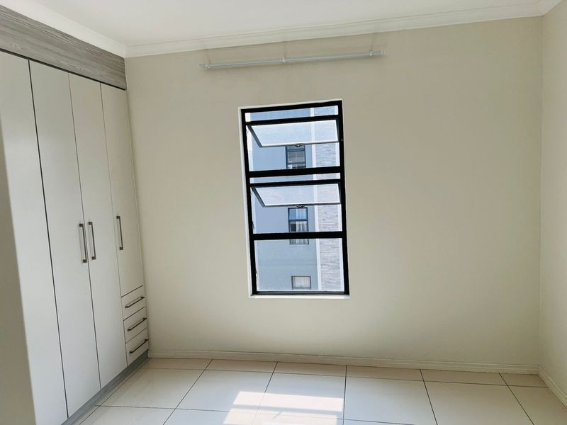 A bright, empty bedroom featuring neutral tiled flooring, built-in cabinetry with integrated drawers, and a modern window with black framing.