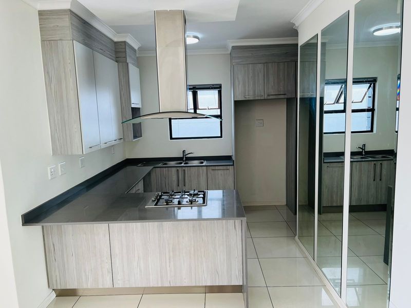 Modern kitchen featuring light wood-grain cabinetry, dark stone countertops, a built-in gas hob, stainless steel extractor fan, and tiled flooring.
