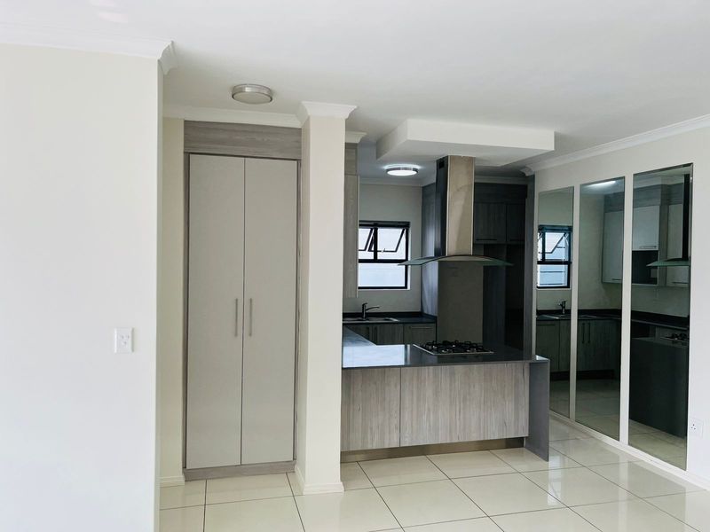 Modern open-plan kitchen featuring sleek cabinetry, a built-in gas hob, stainless steel extractor fan, and polished tile flooring.
