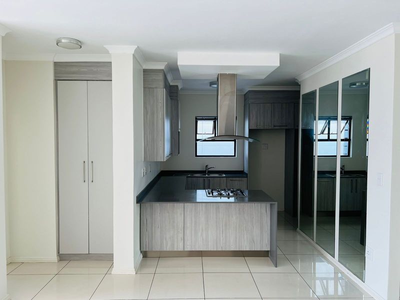 Modern kitchen featuring grey wood-grain cabinetry, dark stone countertops, a built-in gas hob, stainless steel extractor fan, and mirrored built-in cupboards.