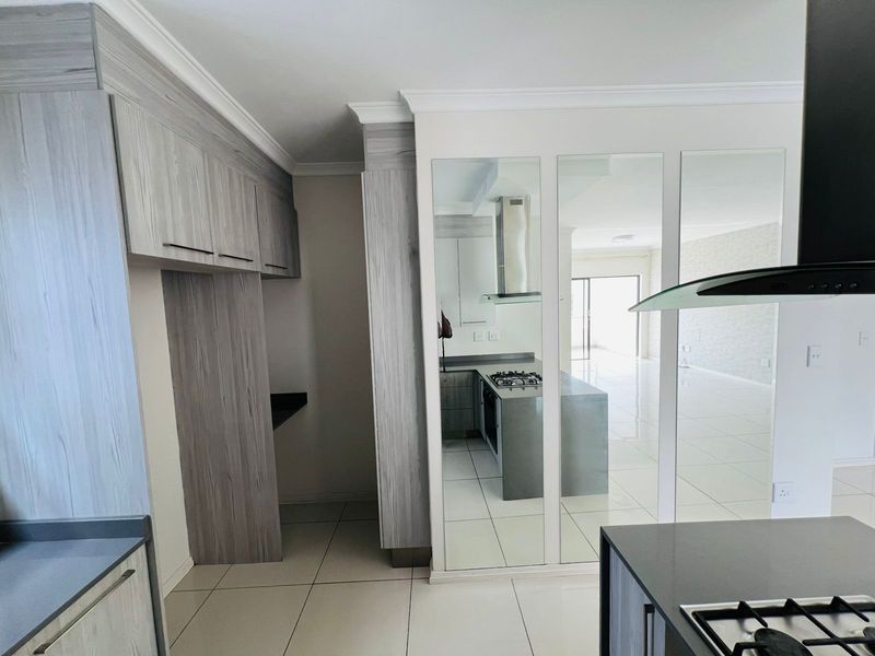 Modern kitchen featuring light wood-grain cabinetry, stone countertops, a built-in gas hob, and an integrated extractor fan, with a mirrored feature wall.
