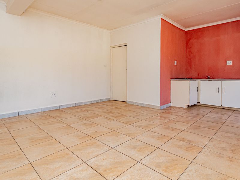 An open-plan living and kitchen area featuring tiled flooring, built-in cabinetry, and a security gate, offering a blank canvas for renovation.