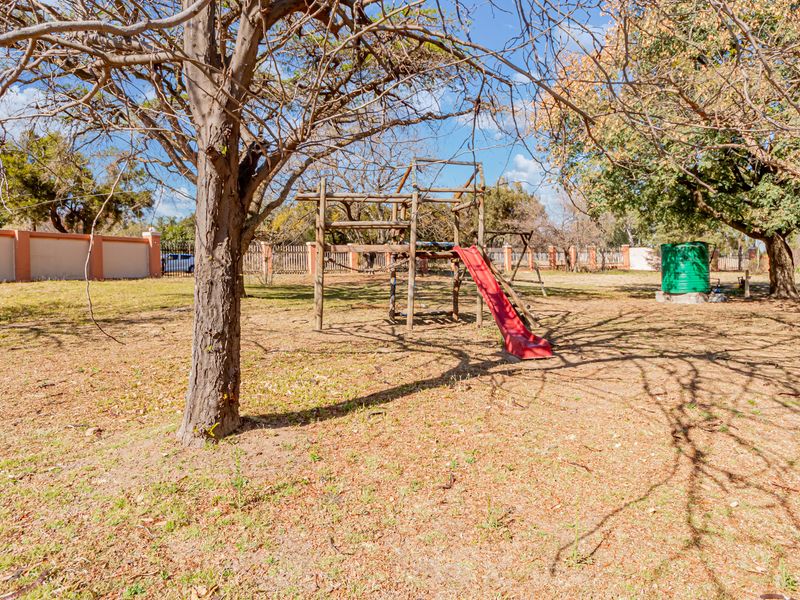 A spacious outdoor garden area featuring mature trees, perimeter walling, and a water storage tank.