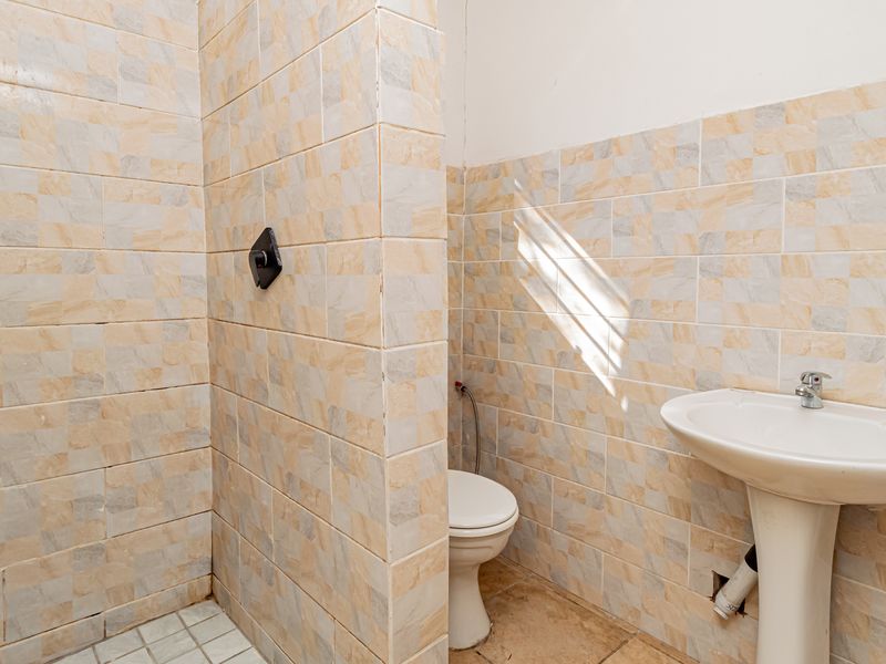 A functional bathroom featuring a pedestal sink, toilet, and a tiled shower enclosure. The space requires cosmetic updates and minor plumbing repairs.