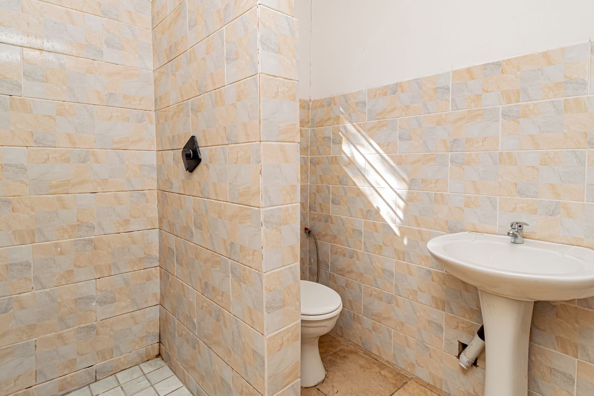 A functional bathroom featuring a pedestal sink, toilet, and a tiled shower enclosure. The space requires cosmetic updates and minor plumbing repairs.