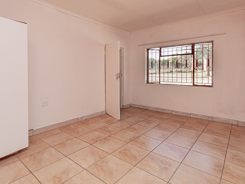A vacant bedroom featuring tiled flooring, a built-in wardrobe, and a window fitted with security bars.