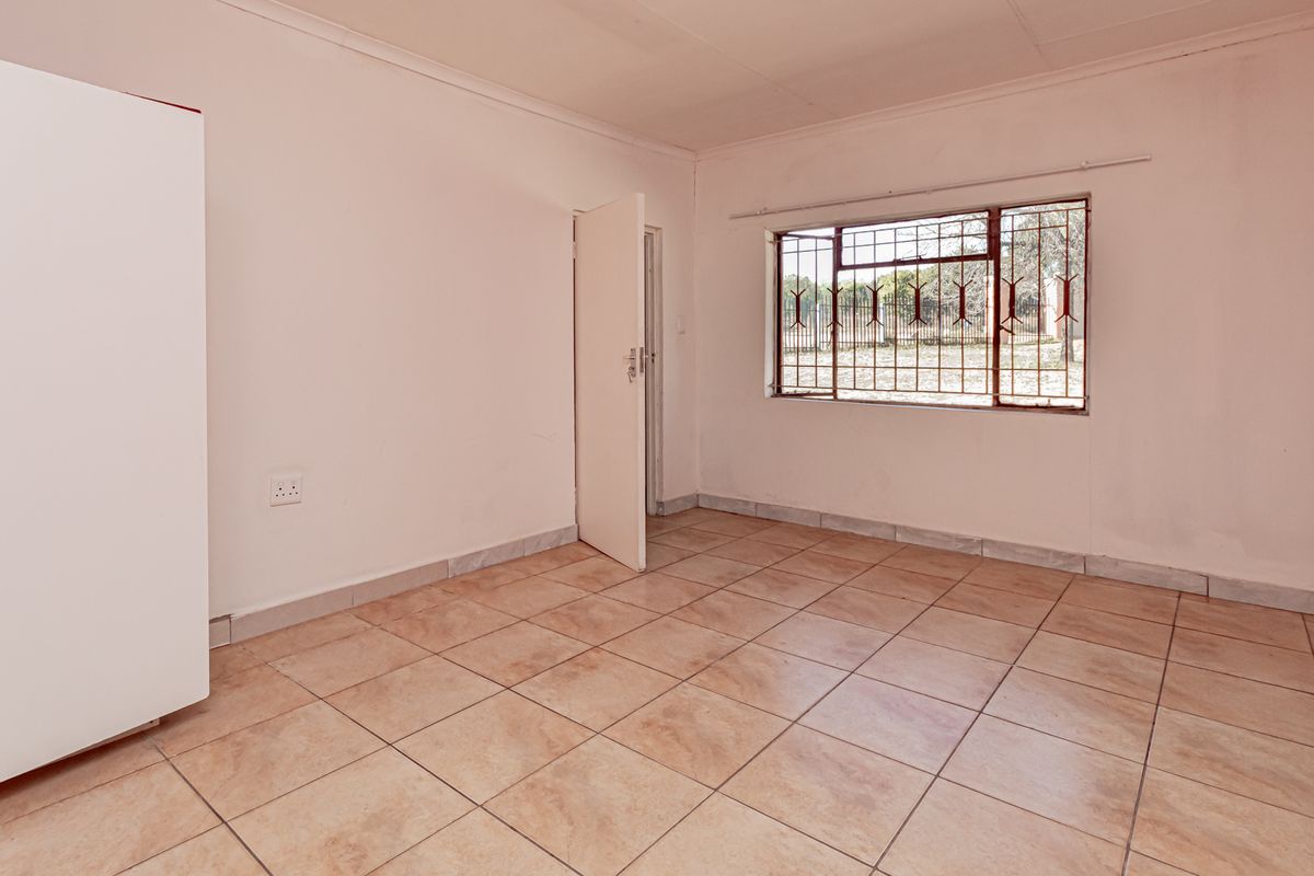 A vacant bedroom featuring tiled flooring, a built-in wardrobe, and a window fitted with security bars.