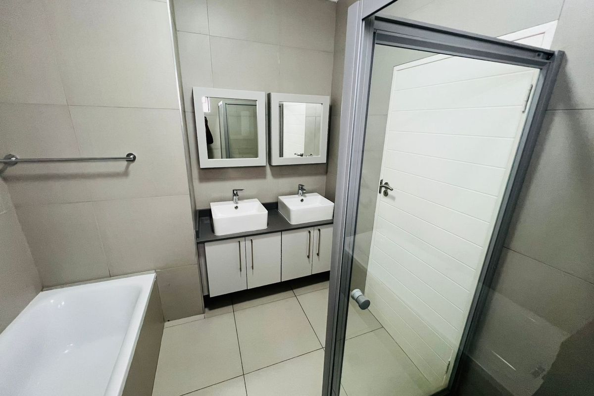 Modern bathroom featuring a double vanity with vessel sinks, a separate bathtub, and a glass-enclosed shower with neutral wall and floor tiling.