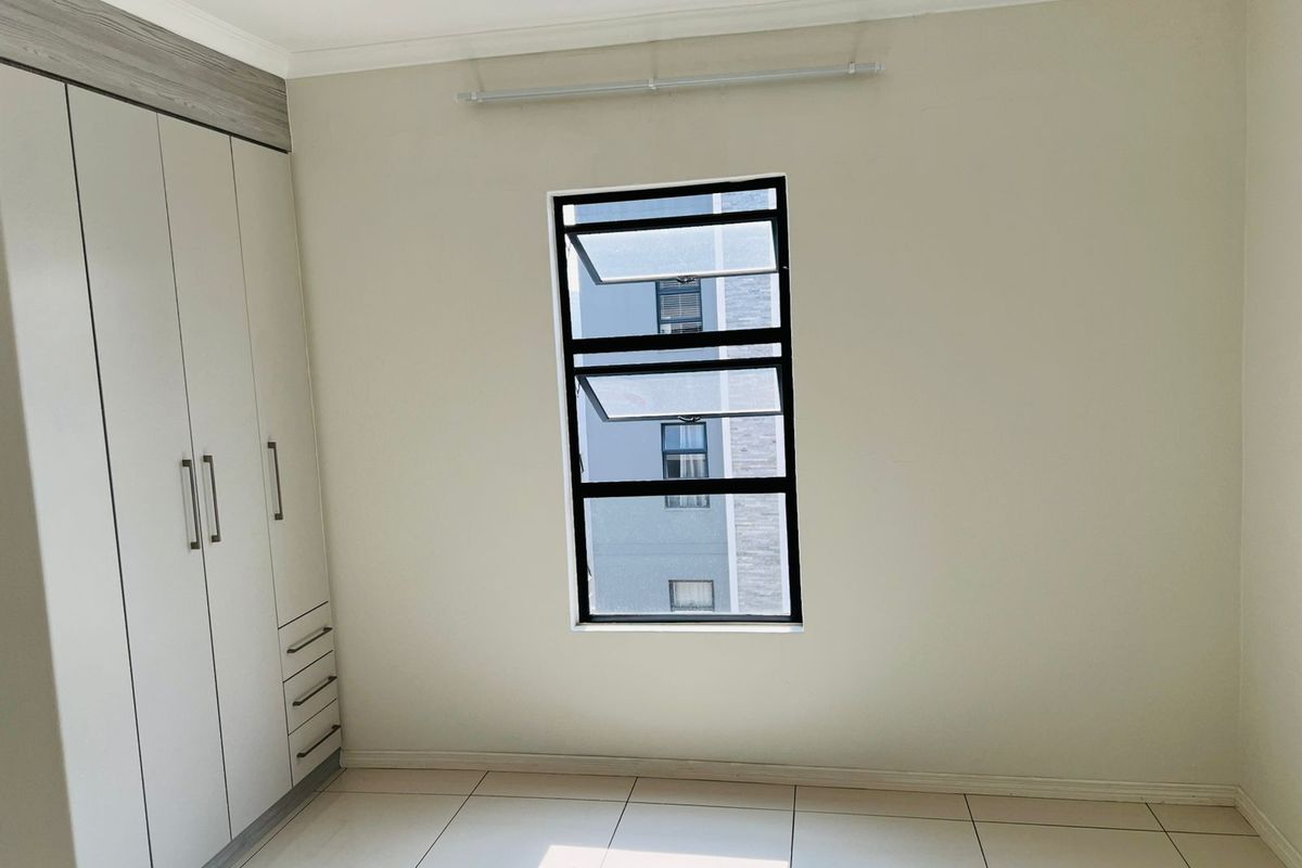 A bright, empty bedroom featuring neutral tiled flooring, built-in cabinetry with integrated drawers, and a modern window with black framing.