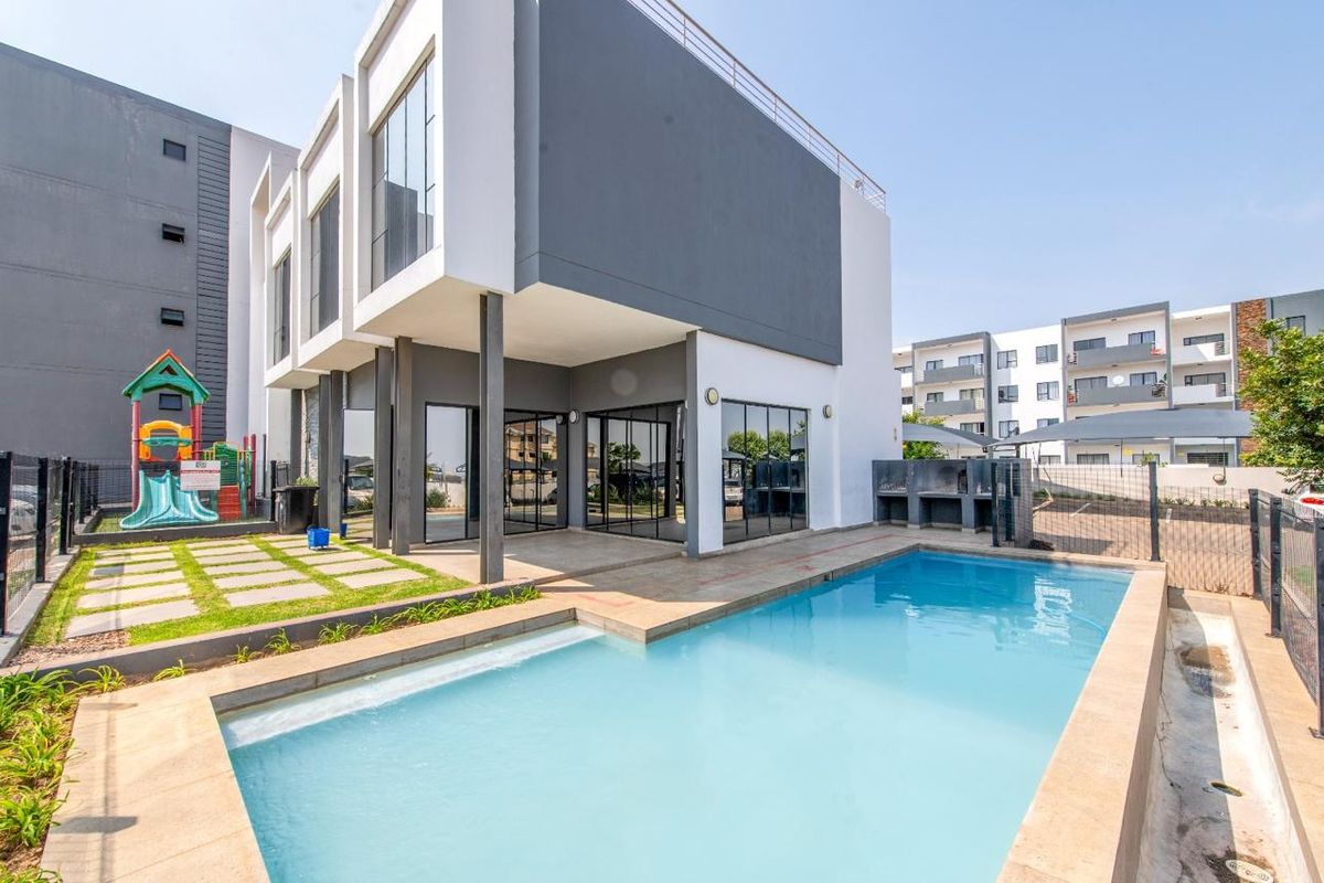 Modern apartment complex exterior featuring a private swimming pool, paved patio area, and built-in outdoor braai facility.