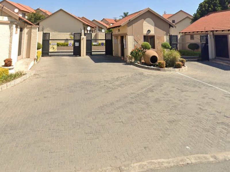 The entrance to the townhouse complex features a secure gated access point, a guard house, and a well-maintained paved driveway.